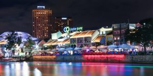 Vista noturna de Clarke Quay em Singapura, com luzes coloridas refletidas no rio e edifícios animados à beira da água